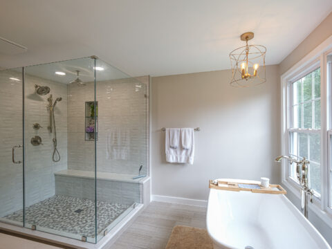 Elegant bathroom with a glass-enclosed shower and freestanding bathtub by a large window.