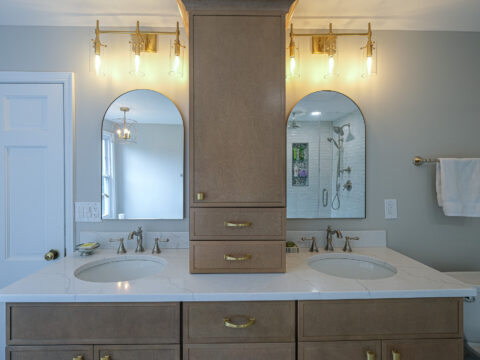 Double-sink vanity with oak cabinetry and two oval mirrors in a modern bathroom.