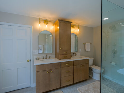 Bathroom vanity with oak cabinets, dual sinks, and brass light fixtures.