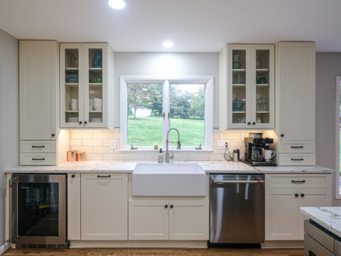 Modern kitchen sink area with white cabinetry, glass doors.
