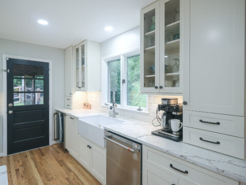 Modern kitchen sink area with a farmhouse sink, white cabinets, and a coffee station.