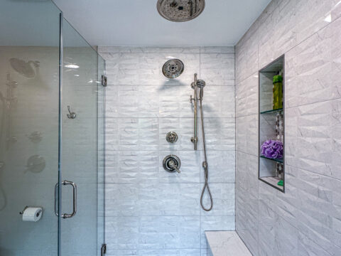 Showerhead and fixtures in a tiled walk-in shower with hexagonal floor tiles.