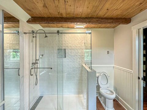 Shower area with glass enclosure and rain shower head in a remodeled bathroom.